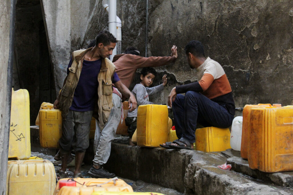 Women and children wait to fill jerrycans with drinking water from a charity tank in Taiz
